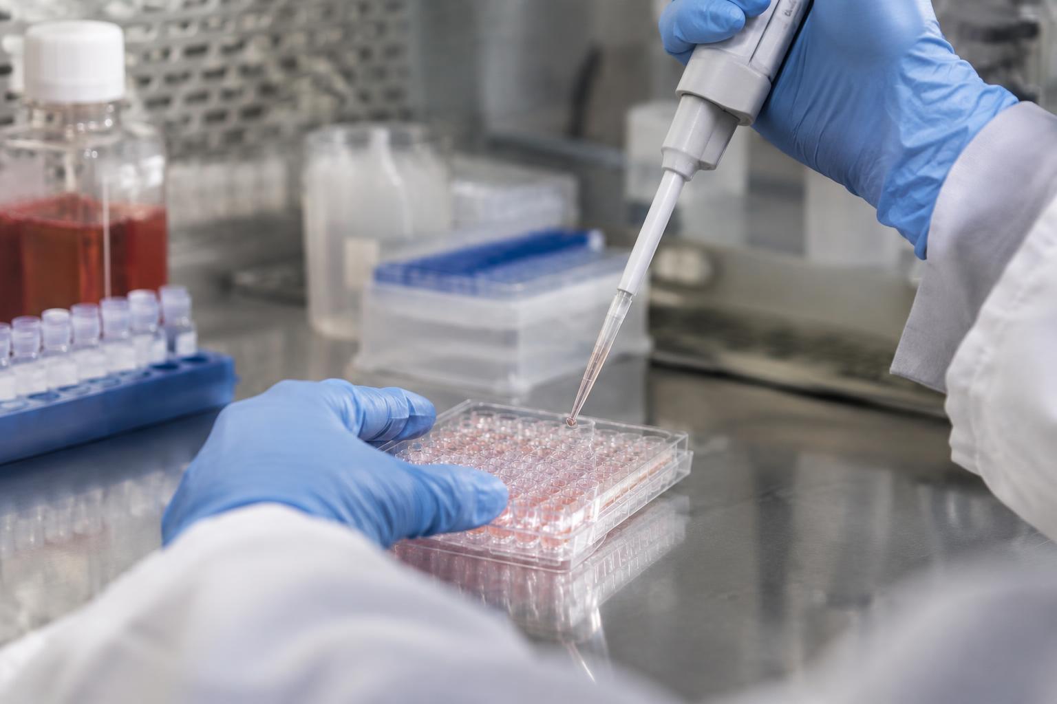 Illustrationsbild av handskbeklädda händer som pipetterar i en laboratorieplatta.